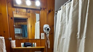 Une salle de bain avec un intérieur en bois, un lavabo blanc, un miroir, un sèche-cheveux et un rideau de douche.