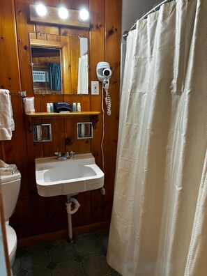 A bathroom with a wooden interior, a white sink, a mirror, a hairdryer, and a shower curtain.