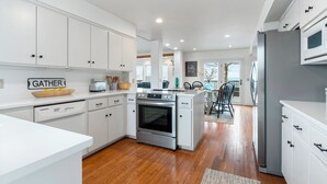 A modern kitchen with white cabinetry, a stainless steel oven, a refrigerator, and a dining area with a view. - Bluff View House has vast open water views of Greers Ferry Lake in Arkansas (Quitman)