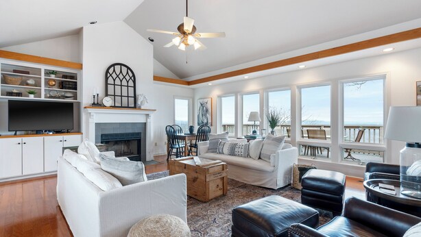 A spacious living room with a fireplace, white sofas, a coffee table, and a view of the ocean. - Bluff View House has vast open water views of Greers Ferry Lake in Arkansas (Quitman)