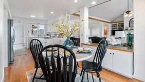 A modern kitchen with white cabinets, a dining area with a round table and black chairs, and a vase with yellow flowers. - Bluff View House has vast open water views of Greers Ferry Lake in Arkansas (Quitman)