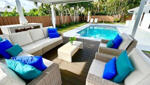 A covered outdoor seating area with wicker furniture and a pool in the background. - `Once upon a Tide`  North Palm 3BR/2B/Heated Pool (North Palm Beach)