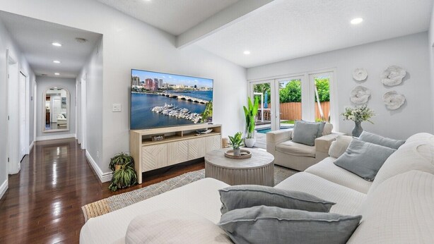 A modern living room with a large TV, a sofa, a coffee table, and a view of a pool and greenery. - `Once upon a Tide`  North Palm 3BR/2B/Heated Pool (North Palm Beach)