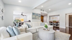 A modern living room with a sectional sofa, a round coffee table, and a dining area with a wooden table and chairs. - `Once upon a Tide`  North Palm 3BR/2B/Heated Pool (North Palm Beach)