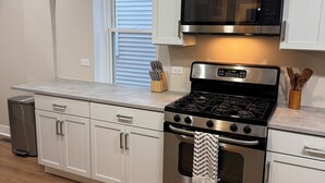 Een moderne keuken met witte kastjes, een roestvrijstalen fornuis, een magnetron en een raam met luxaflex.