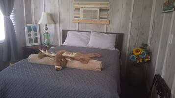 A bed with a patterned bedspread, a decorative headboard, a wall-mounted air vent, and a vase with flowers.