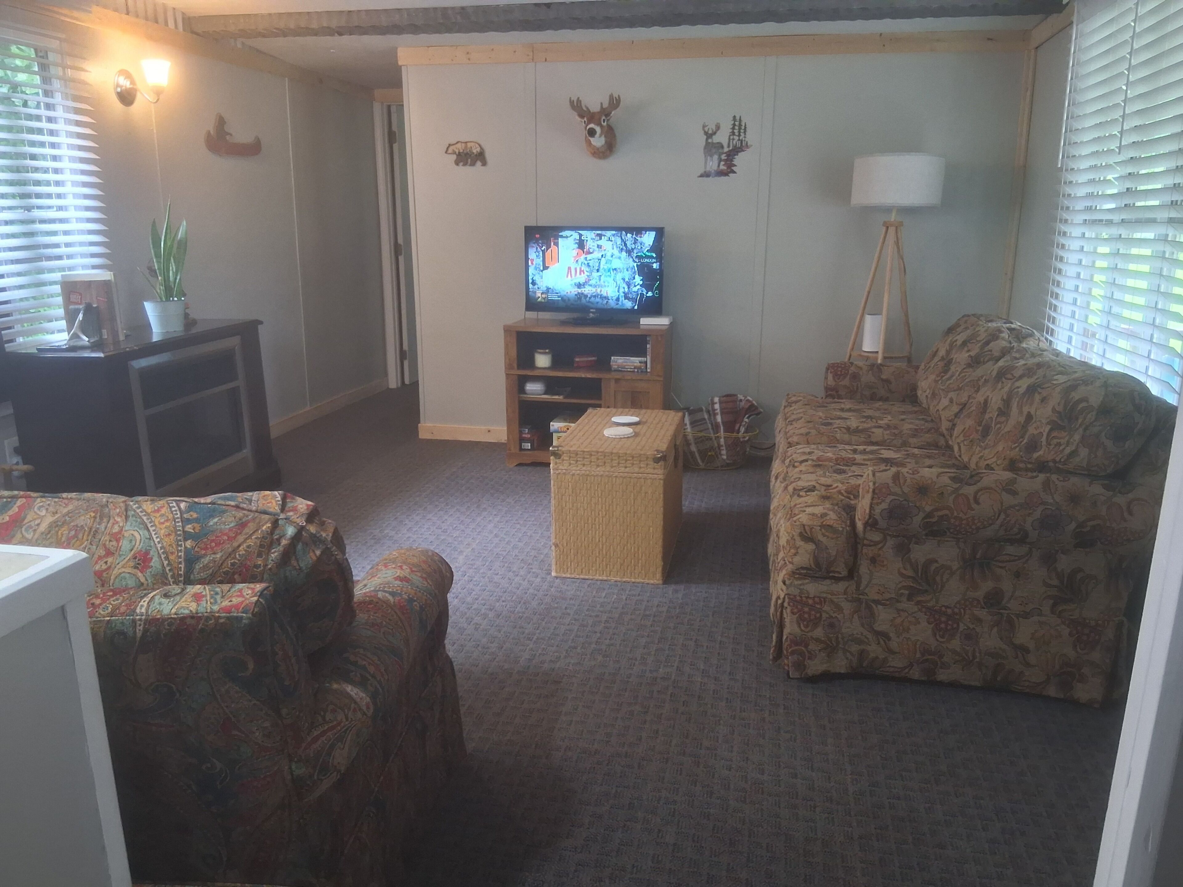 A living room with a television, a sofa, a patterned armchair, a small table, and wall decorations including animal figures.
