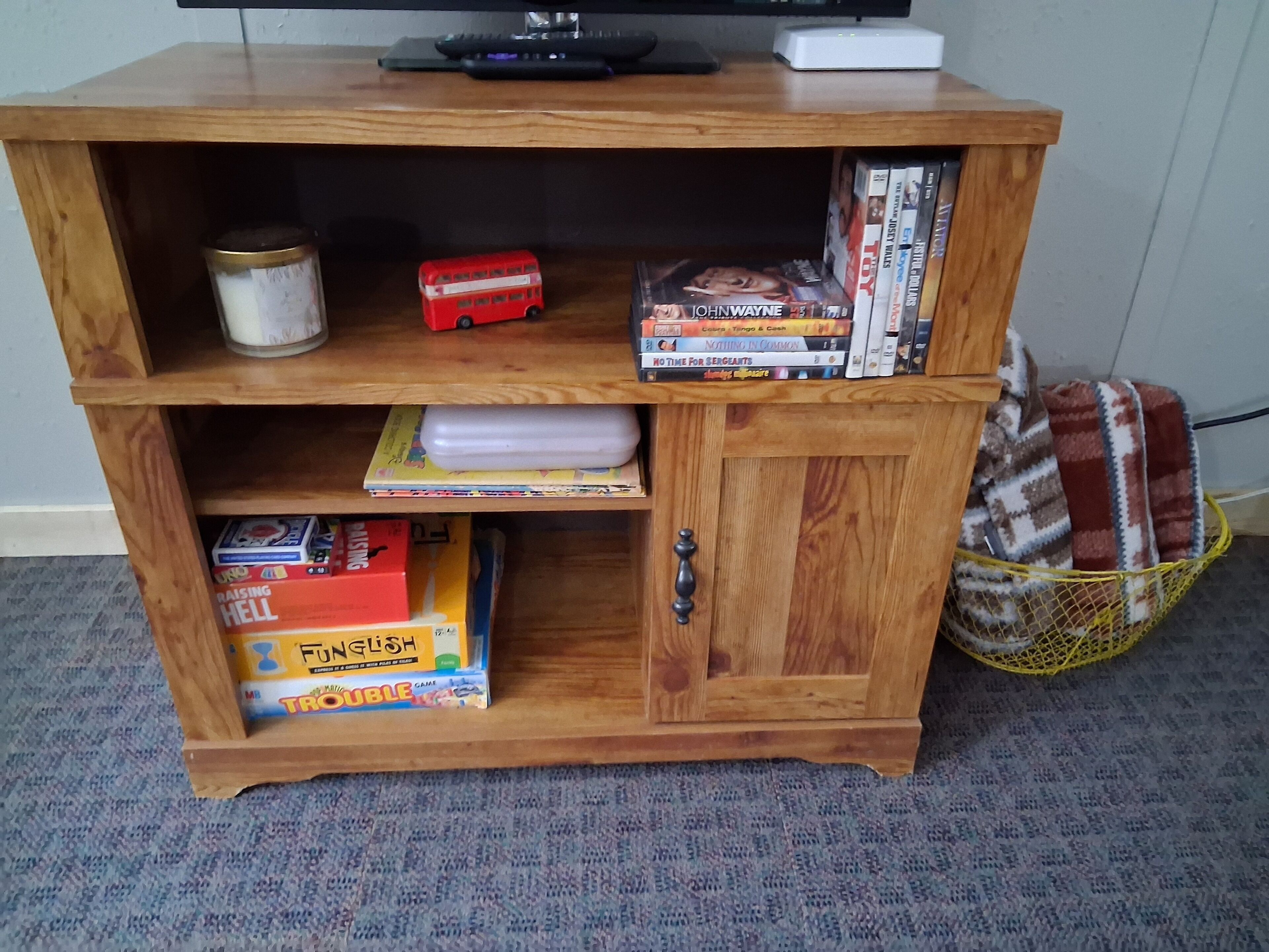 Una estantería de madera con diversos objetos, incluyendo libros, un reproductor de DVD y una pequeña maqueta de autobús rojo.