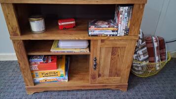 Una estantería de madera con diversos objetos, incluyendo libros, un reproductor de DVD y una pequeña maqueta de autobús rojo.