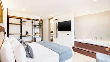 Camera da letto moderna con un letto, comodini, TV, doccia idromassaggio e un piccolo angolo salotto.