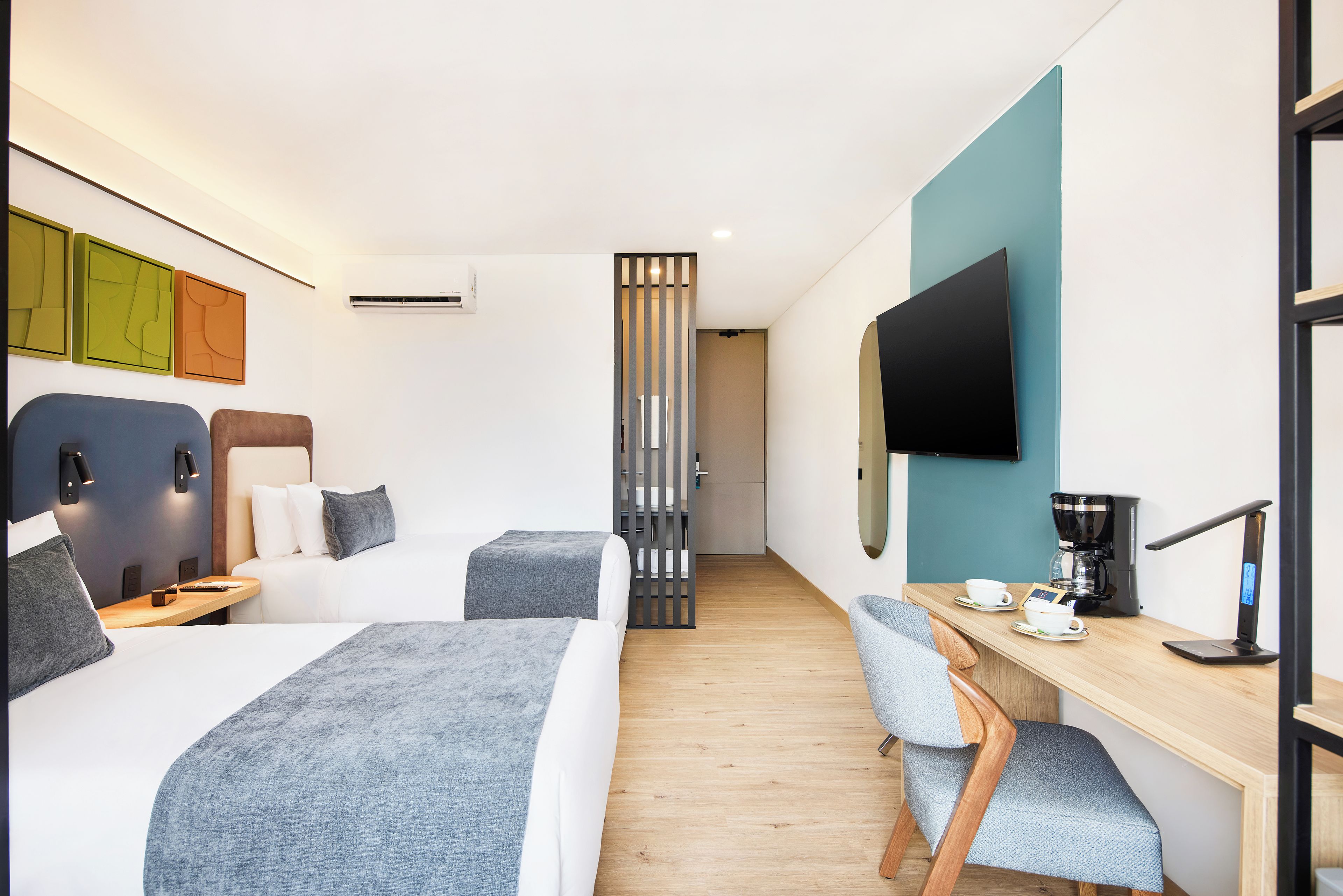 Ein Hotelzimmer mit Bett, Nachttischen, Schreibtisch mit Stuhl, Kaffeemaschine und Wandfernseher.