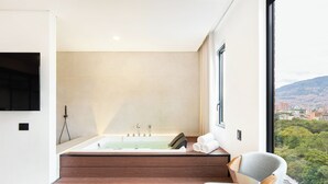 A modern bathroom with a freestanding bathtub, a wooden bench, and a view of a cityscape through a large window.