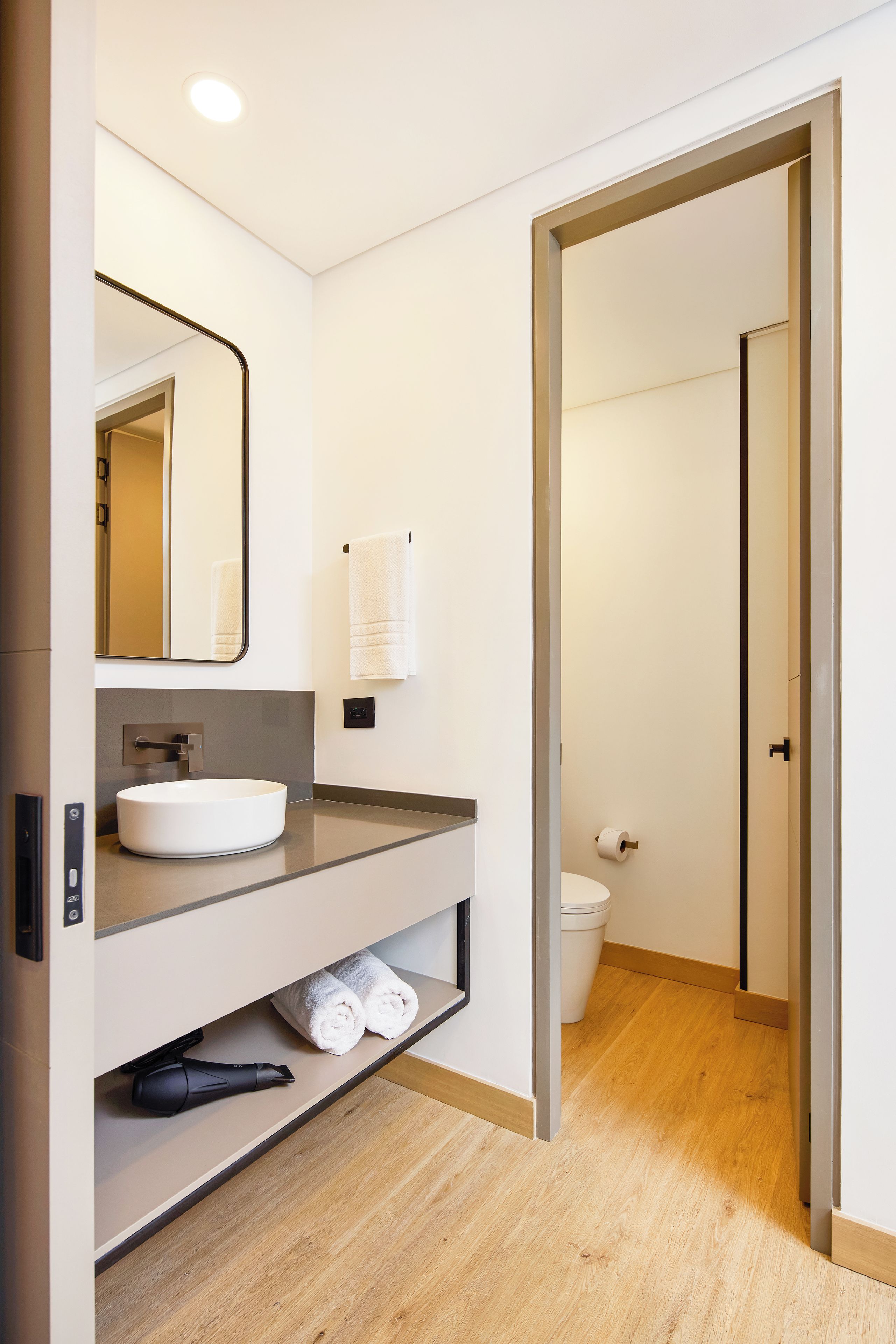 Un baño moderno con lavamanos, espejo y toallero blancos.