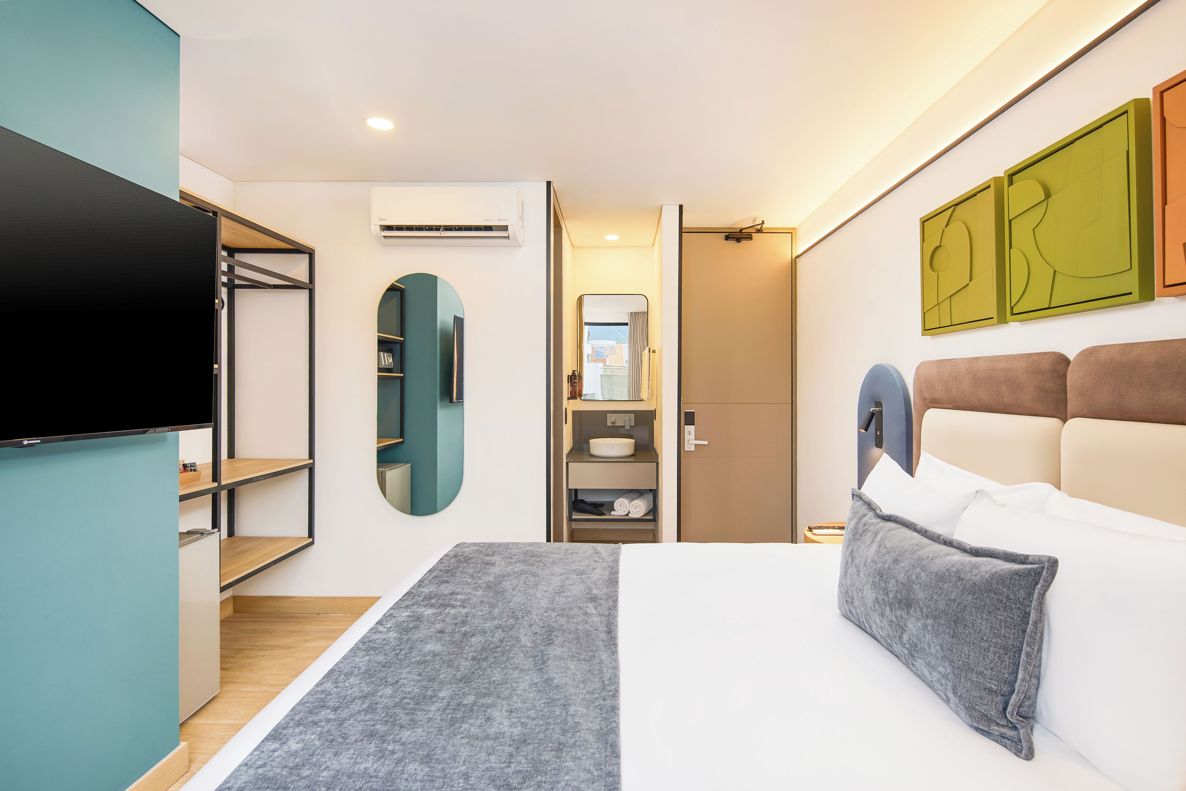 A modern hotel room with a bed, a TV, a wardrobe, and a bathroom.