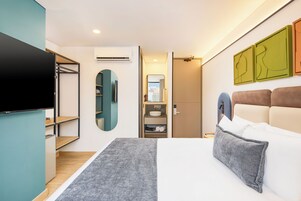 A modern hotel room with a bed, a TV, a wardrobe, and a bathroom.
