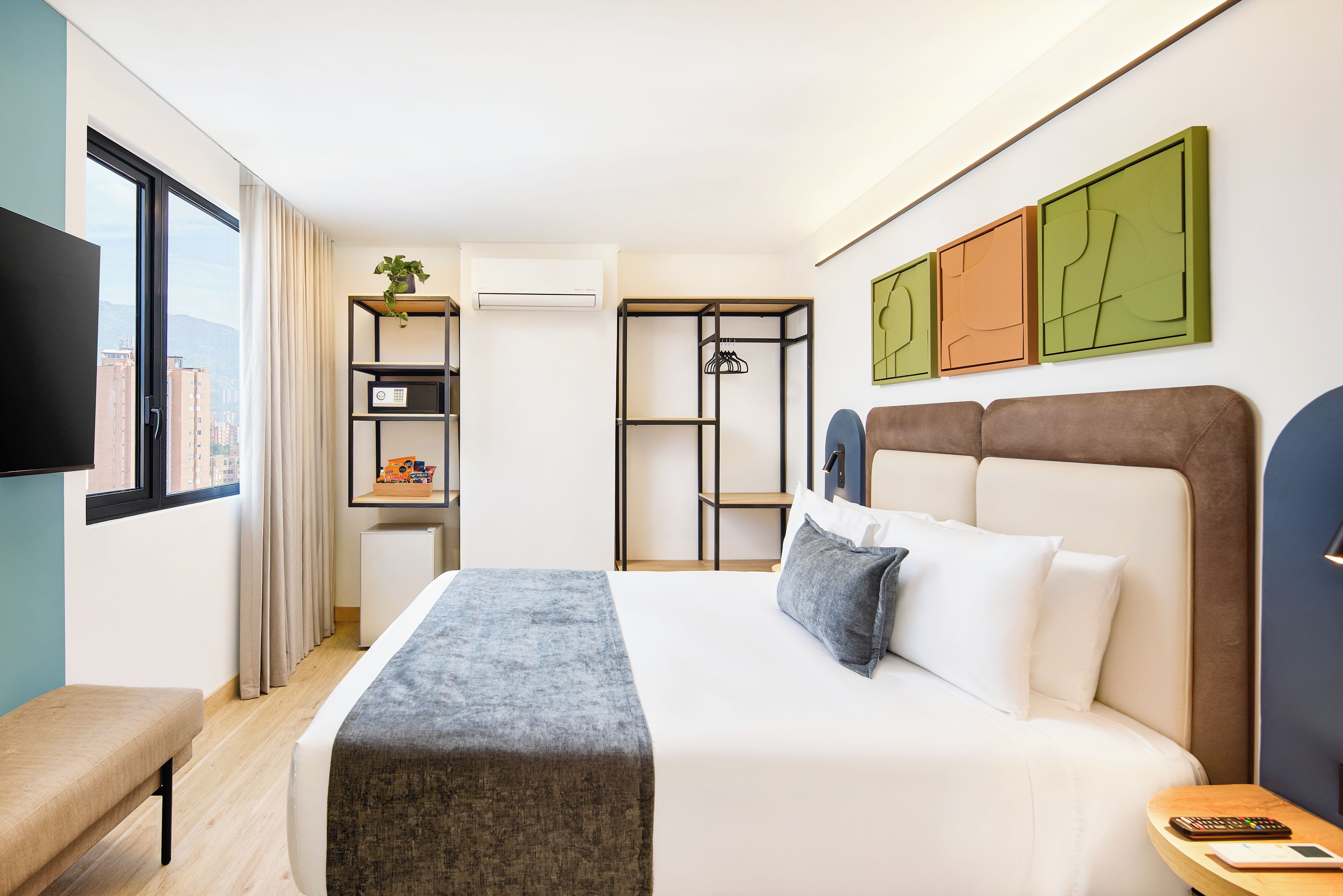 A hotel room with a bed, a bench, a TV, a wardrobe, and a window with curtains.