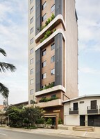 A multi-story building with balconies, a ground-level entrance, and surrounding greenery.