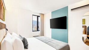Une chambre d’hôtel équipée d’un lit, d’un téléviseur fixé au mur, d’une fenêtre donnant sur la ville et d’un climatiseur fixé au mur.