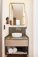Un baño moderno con un lavabo redondo, un espejo y un perchero para toallas.