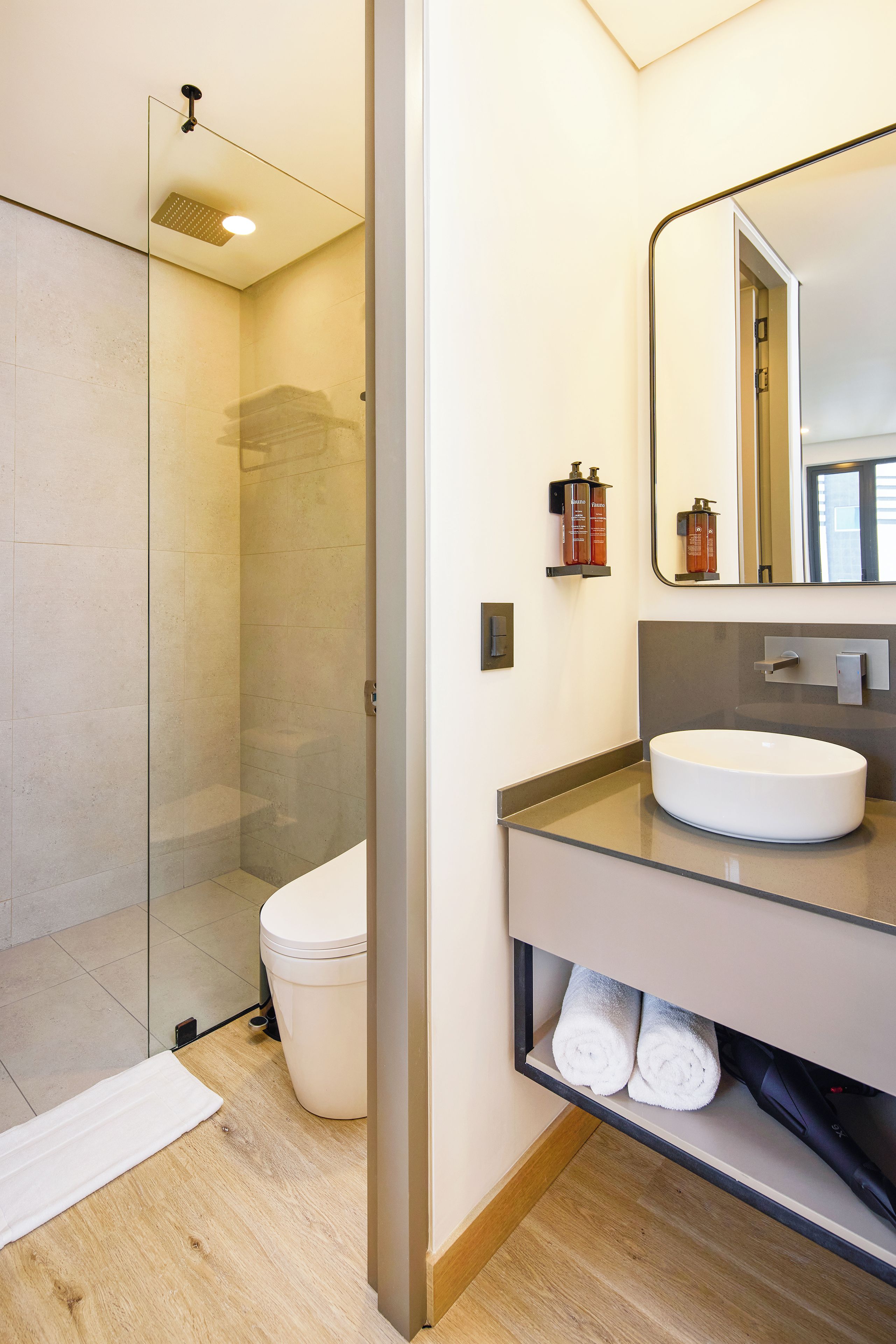 Een moderne badkamer met een douchecabine van glas, een wit toilet, een wastafel met spiegel en een handdoekhouder.