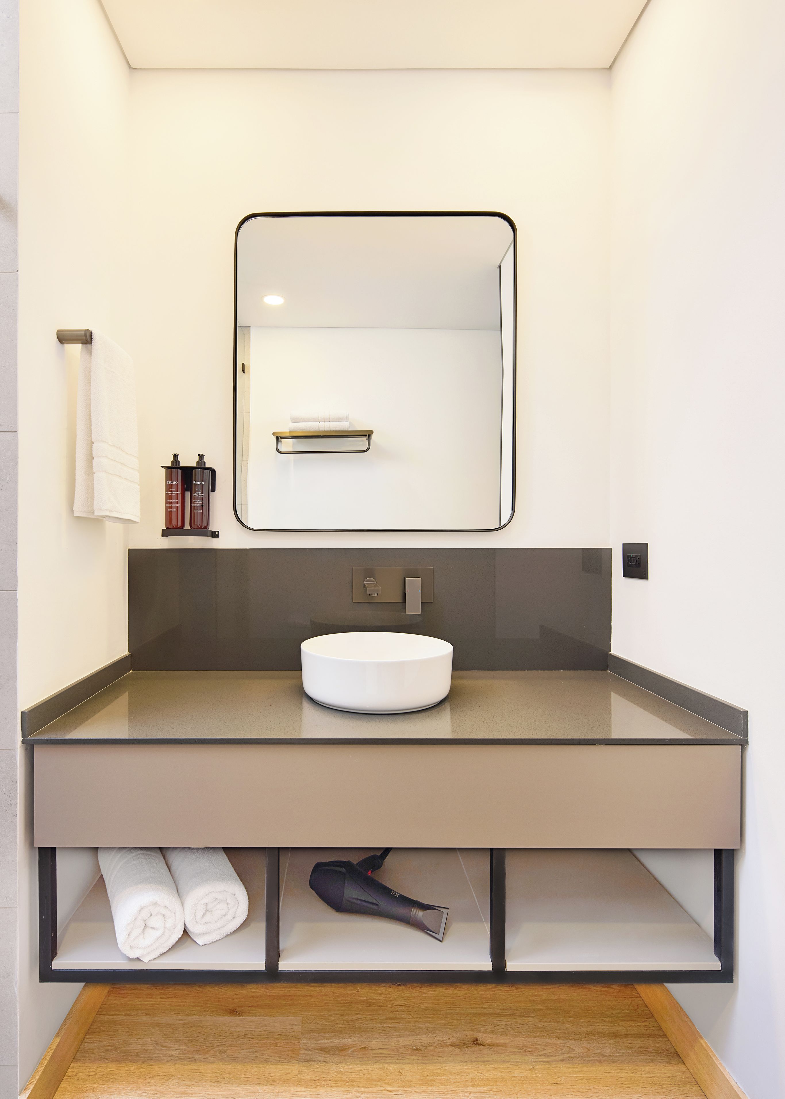 A modern bathroom with a large mirror, a round sink, and a towel rack.