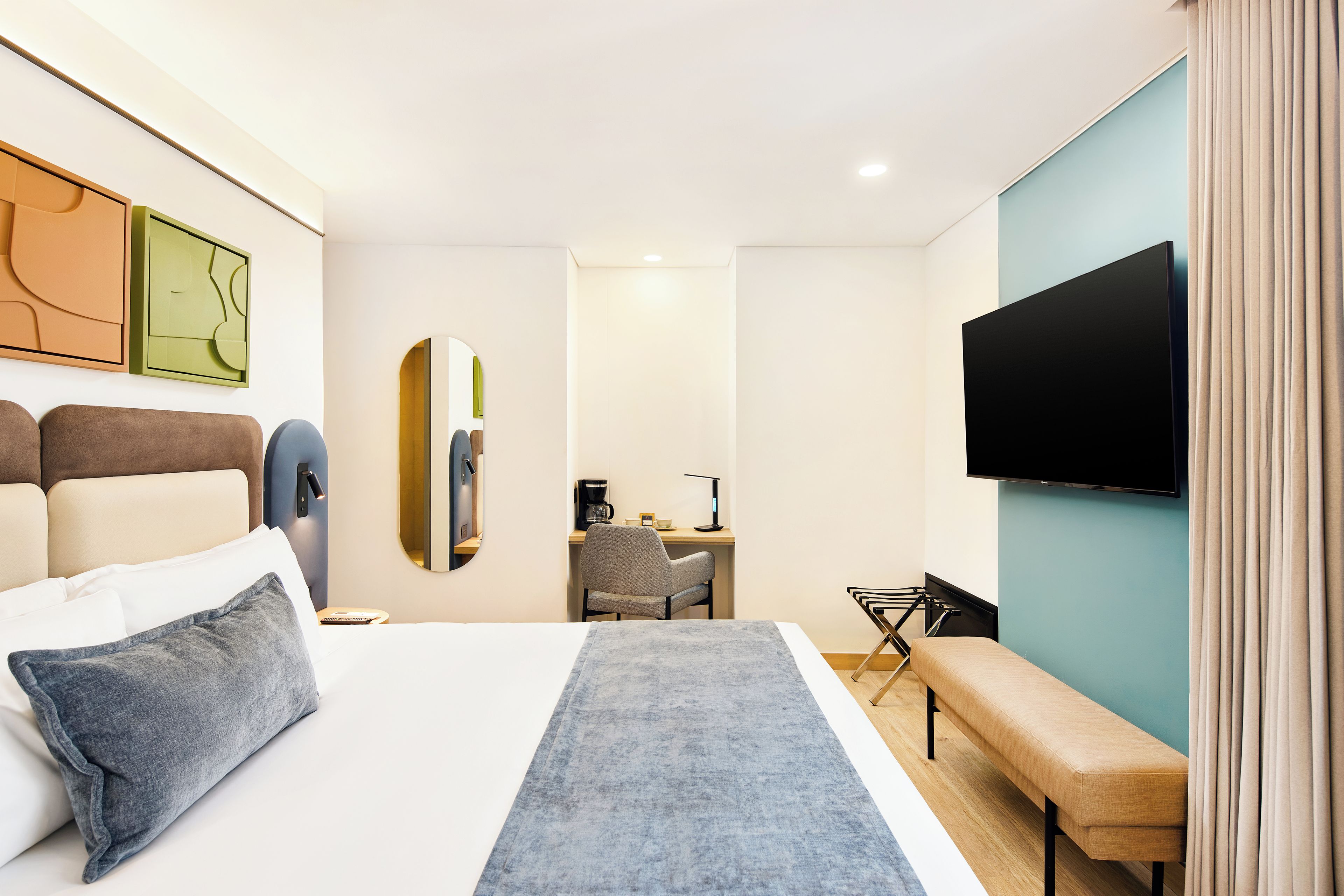 Una habitación de hotel con cama, escritorio, silla, televisor y una banca.