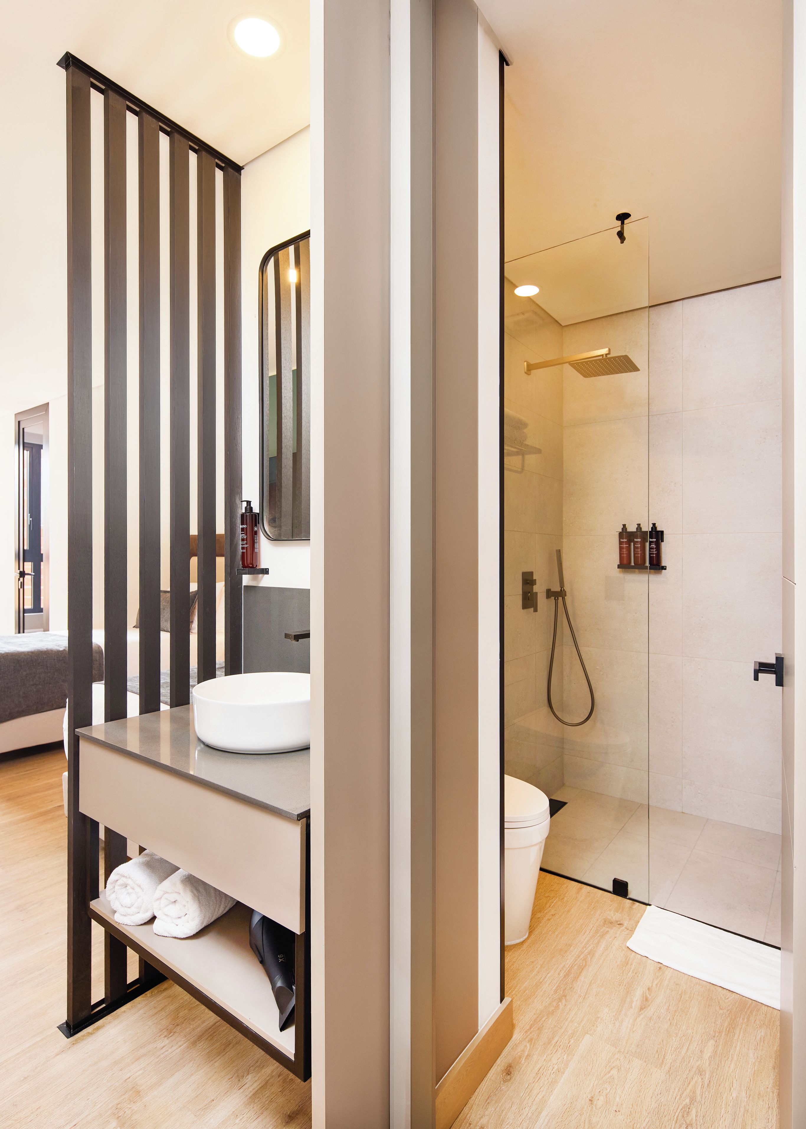 Un baño moderno con cabina de ducha de vidrio, un lavamanos blanco y suelo de madera.