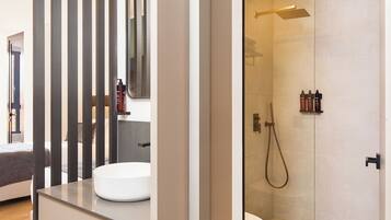 Un baño moderno con cabina de ducha de vidrio, un lavamanos blanco y suelo de madera.