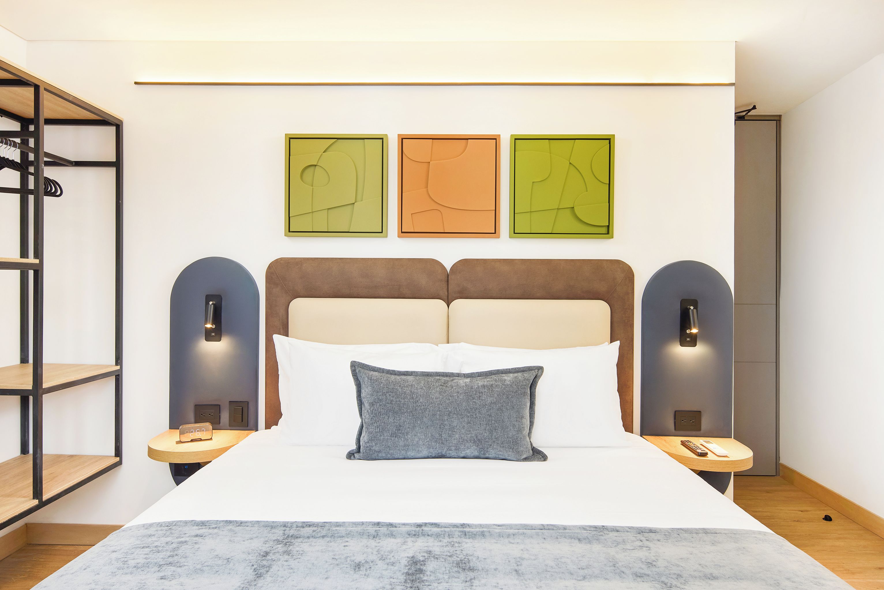 Un dormitorio moderno con una cama, una mesita de noche, un estante de pared y tres obras de arte abstracto en la pared.