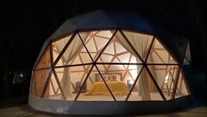 Estructura de domo geodésico con una cama y cortinas visibles en su interior.