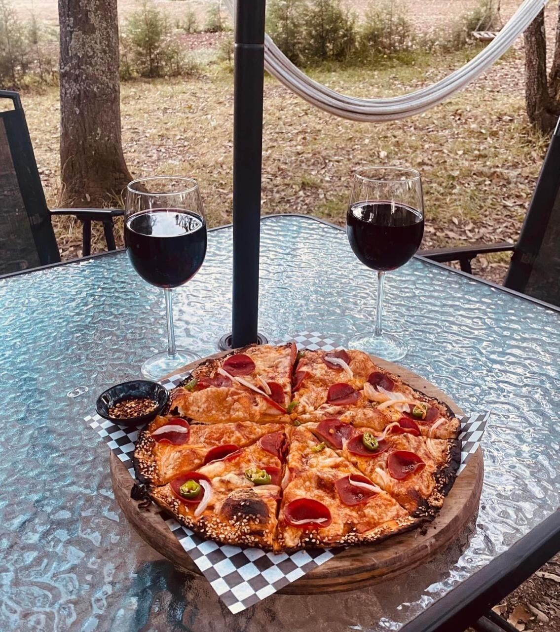 A pizza on a glass table with two glasses of red wine.