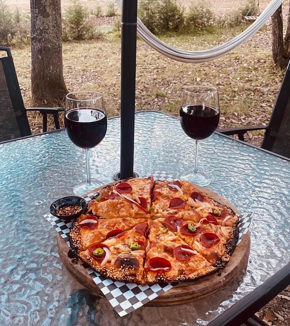 A pizza on a glass table with two glasses of red wine.