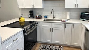 A modern kitchen with white cabinets, a black stove, a yellow kettle, and a stainless steel sink. - Welcome to Heidi's Nest! Renovated 2BR Condo in Bradenton Beach/Runaway Bay! (Bradenton Beach)