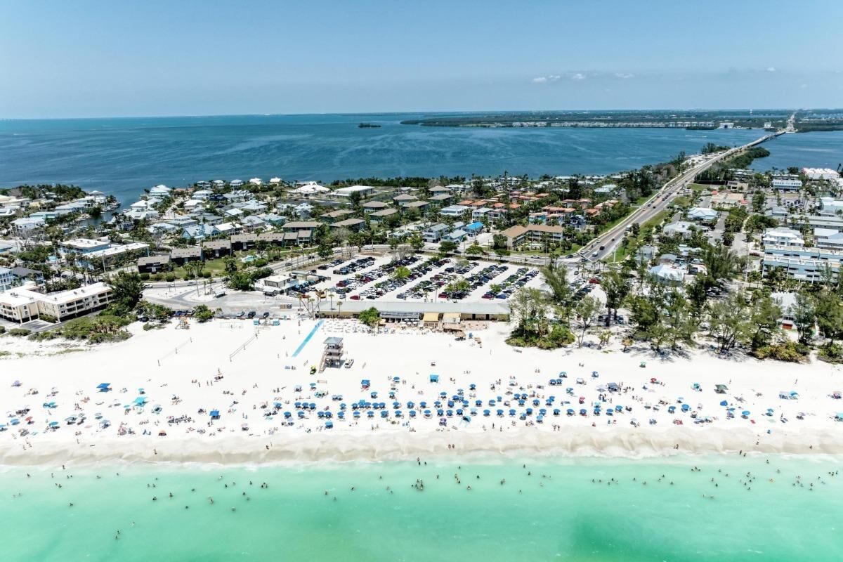 An aerial view of a coastal town with a beach, parking areas, and a road leading to the sea.