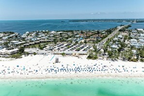 Luftaufnahme einer Küstenstadt mit Strand, Parkplätzen und einer Straße, die zum Meer führt.