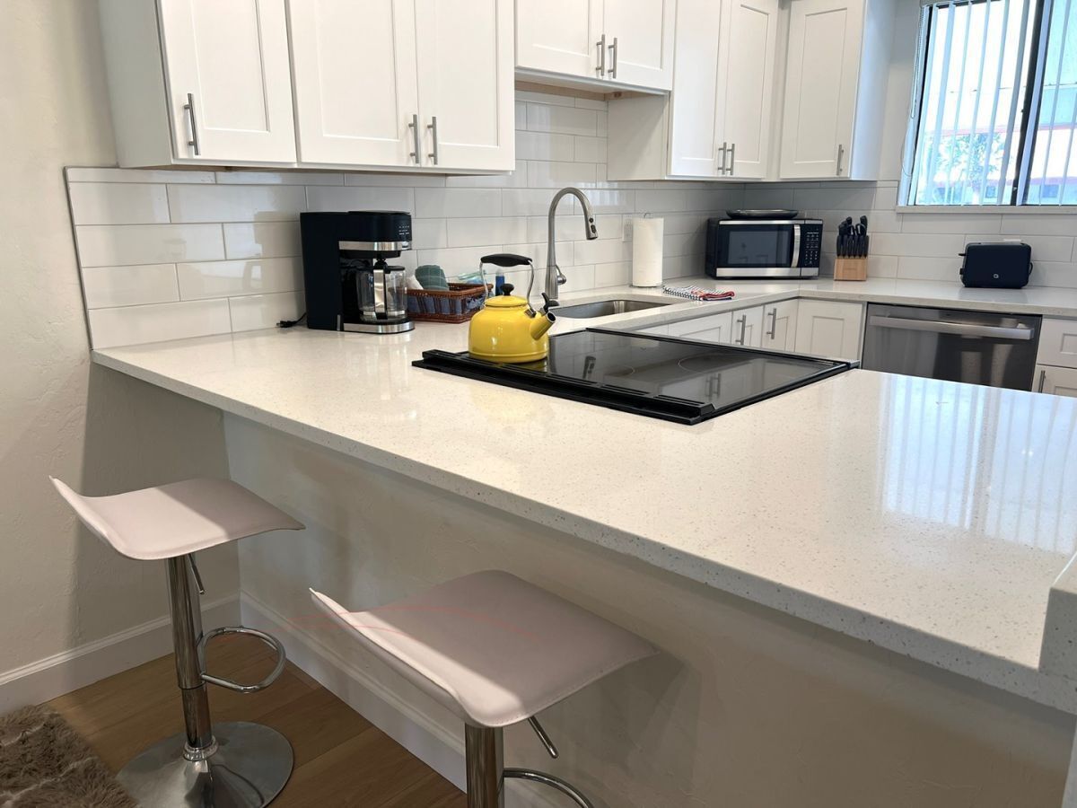 A modern kitchen with white cabinetry, a black countertop, a yellow kettle, and a built-in microwave.