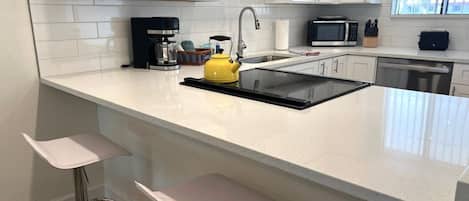 A modern kitchen with white cabinetry, a black countertop, a yellow kettle, and a built-in microwave.