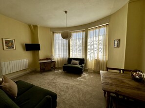 A living room with a green sofa, a wooden table, a television on the wall, and a radiator. - Hidden Georgian Apartment - Central Bath (Bath)