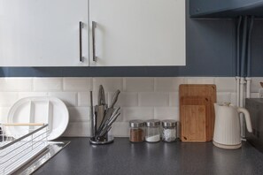 A kitchen with white cabinets, a black countertop, a cutting board, a kettle, and various utensils. - Hidden Georgian Apartment - Central Bath (Bath)