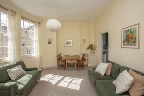 A room with two green sofas, a wooden dining table with chairs, a white ceiling light, and a framed picture on the wall. - Hidden Georgian Apartment - Central Bath (Bath)