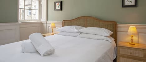 A neatly made bed with white linens and pillows, a window with a view of buildings, and two bedside lamps on wooden nightstands.