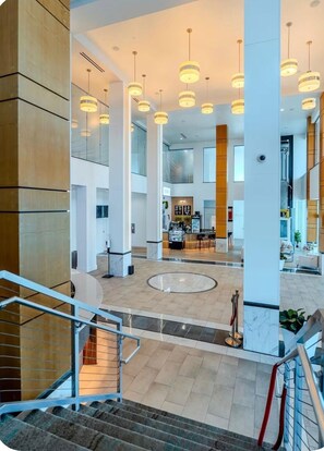 A modern hotel lobby with a central seating area, a reception desk, and a staircase leading to an upper floor. - Luxury Skyline Resort-Style Pool & Gym (Fort Myers)