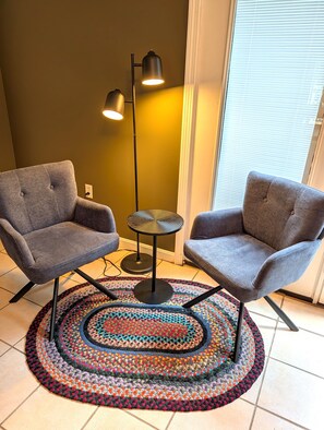 A room with two grey armchairs, a small round table, a colorful crocheted rug, and a tall floor lamp. - Lakeside Haven on Whites Pond (Palmyra)