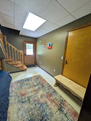 Un couloir avec un banc en bois, une porte, un escalier et un tapis à motifs.