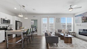 Een moderne keuken met roestvrijstalen apparatuur, een eethoek met barstoelen, een woonkamer met een bank en salontafel, en een open haard.