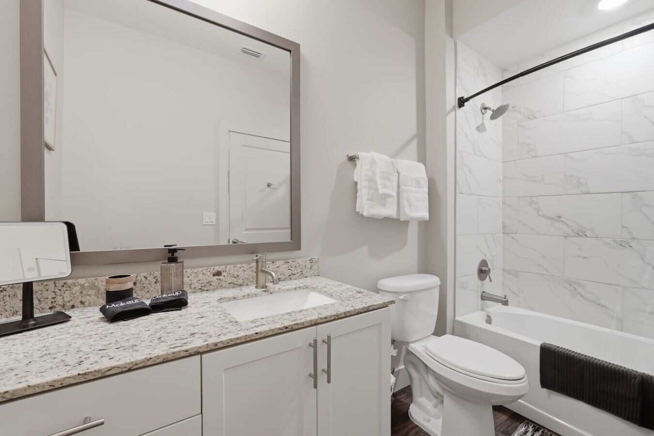 A modern bathroom with a granite countertop, a large mirror, a toilet, and a shower area.