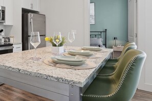 Una cocina con encimera de granito, refrigerador y comedor con una silla tapizada en verde.