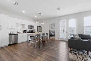 A modern kitchen with white cabinets, stainless steel appliances, and a dining area with bar stools. - Resort-Style 2BR/2BA Mins to Universal & Disney! (Orlando)