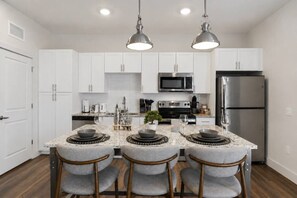A modern kitchen with white cabinets, stainless steel appliances, and a central island with bar stools. - Resort-Style 2BR/2BA Mins to Universal & Disney! (Orlando)