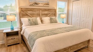 Ein Schlafzimmer mit hölzernem Kopfteil, einem Bett mit weißer Bettwäsche, zwei Nachttischlampen und einem Fenster mit Jalousien.